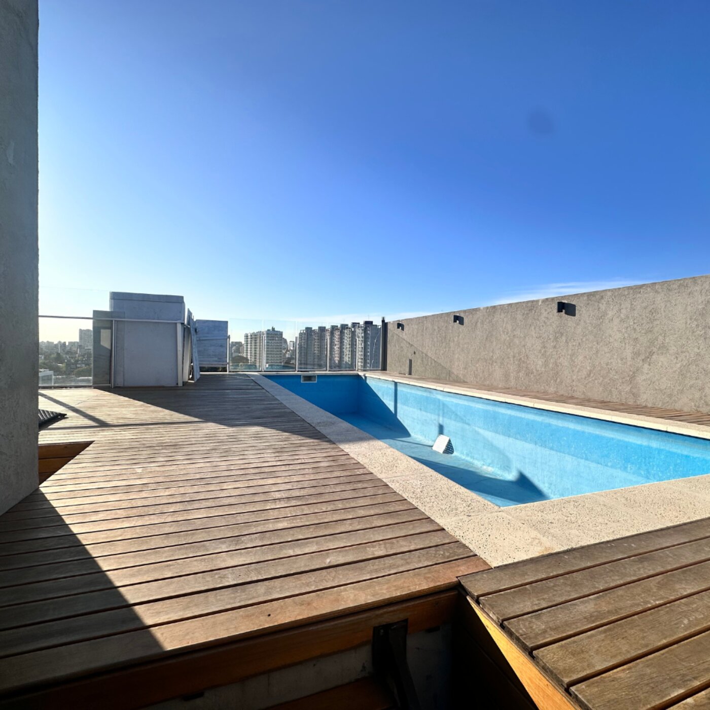 Pileta con solárium y deck de madera en la terraza del edificio