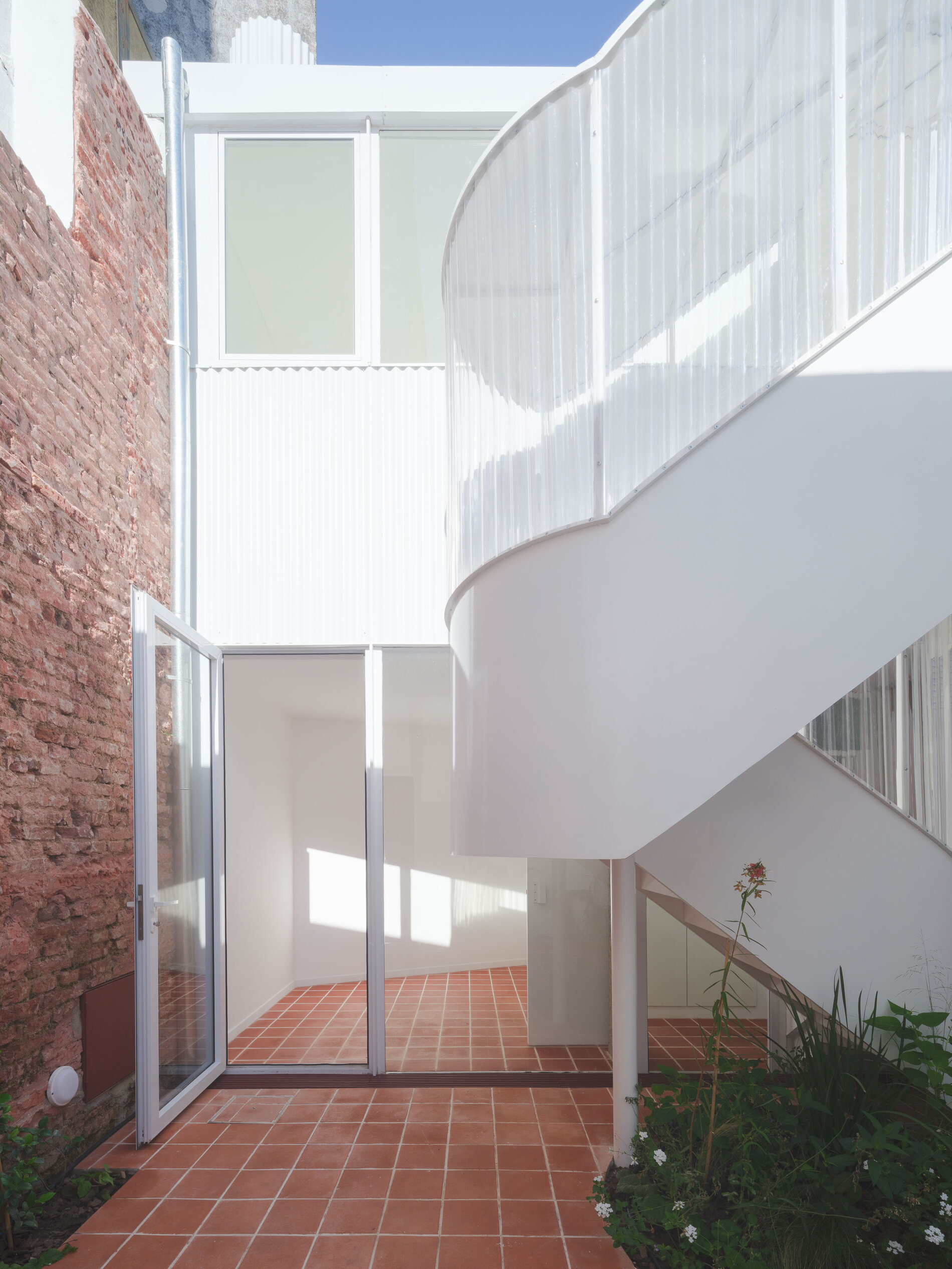 Patio del PH con escalera curva blanca, muro de ladrillo y vegetación