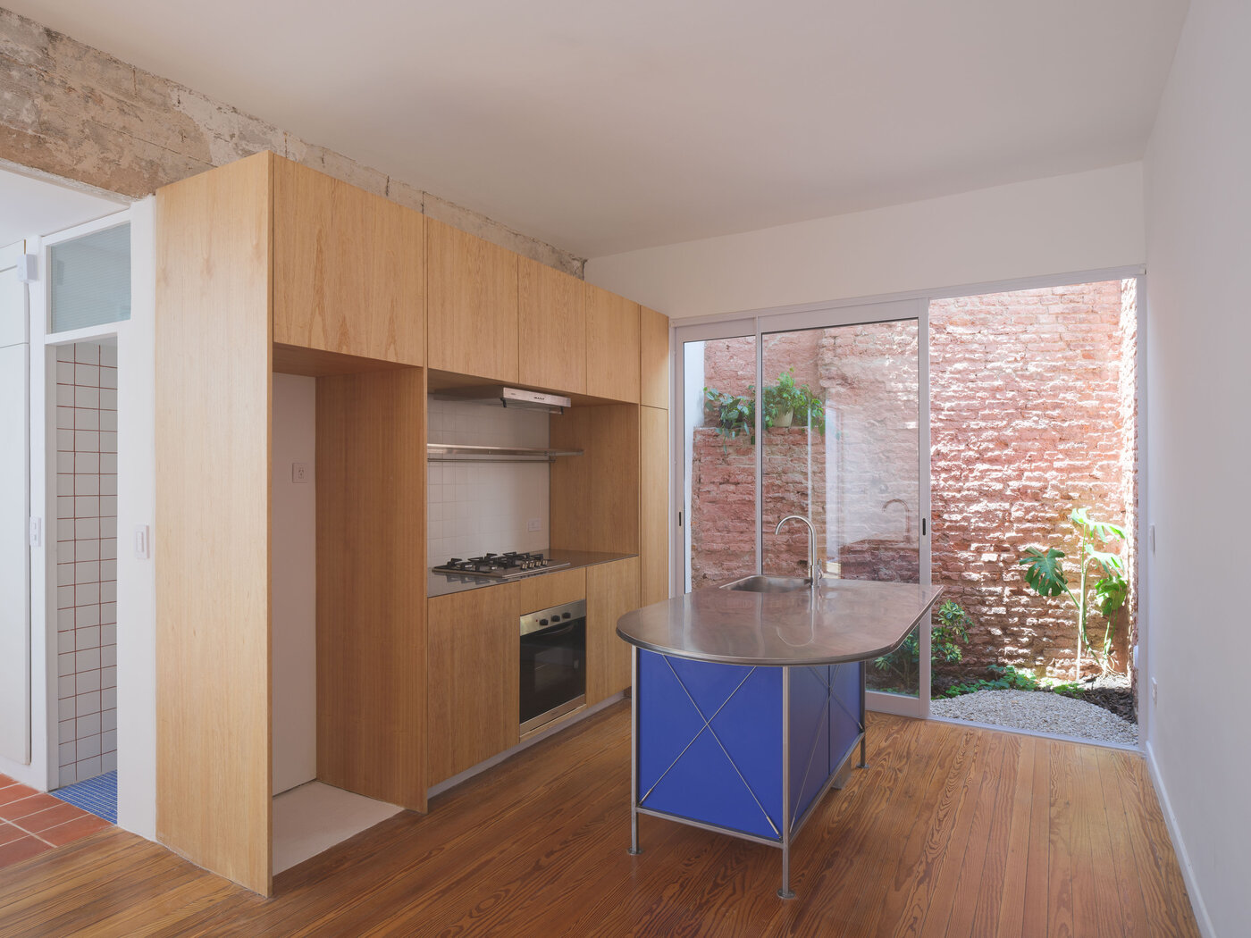 Cocina con muebles de madera kiri e isla de acero, abierta al patio